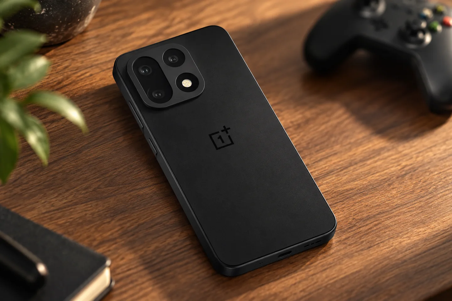 Чёрный OnePlus 15 на деревянном столе рядом с игровым контроллером
